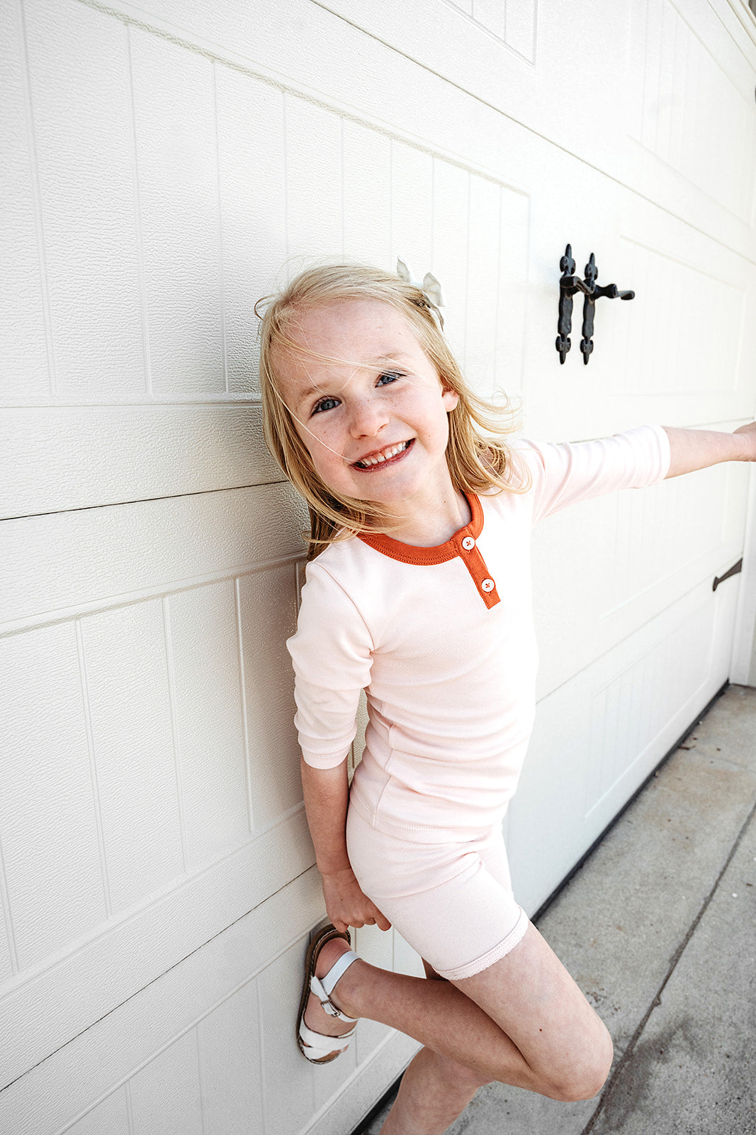kid leaned against cream wall wearing a light pink girls henley and light pink biker shorts in high quality ethically made organic pima cotton.