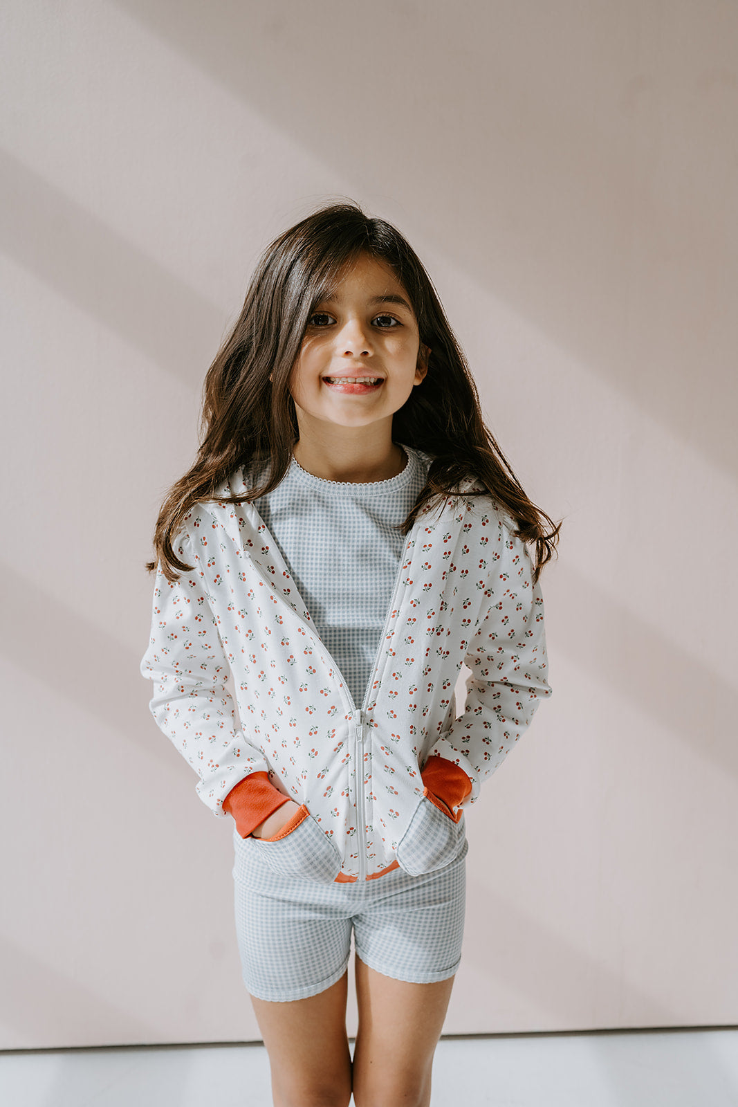 Little girl wearing high quality organic pima cotton cherry zip up hoodie with gingham pockets and gingham girls biker shorts.