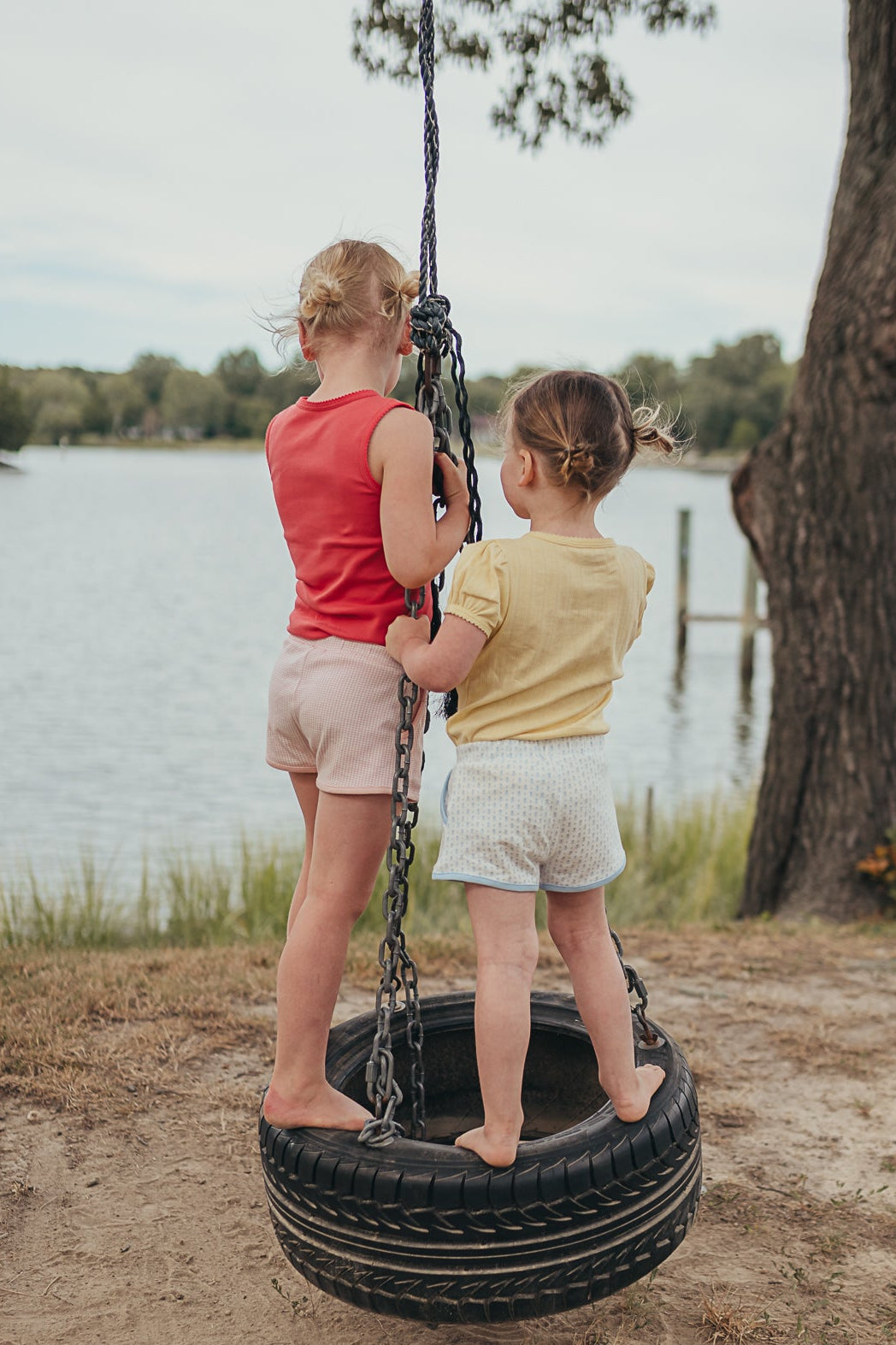Two children on a tire swing by a lake