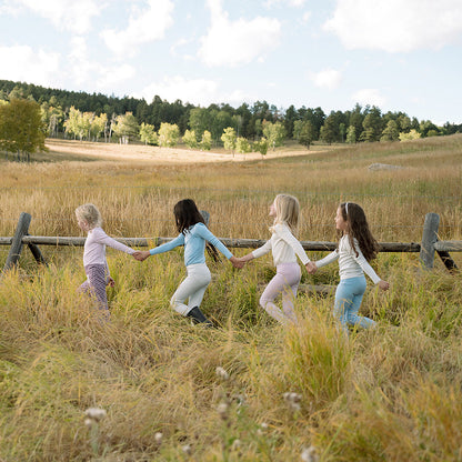 Four little girls holding hands walking along a wooden fence wearing organic pima cotton kids clothing.